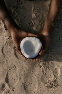 Hands holding fresh coconut in beach sand at TAWC ritual
