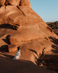 bride and groom walking through the desert next to large rock formations