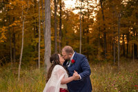 Bride and groom kiss at sunset surrounded by warm colors from fall foliage
