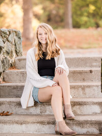 Blonde high school senior girl leans on a pillar during senior portrait session