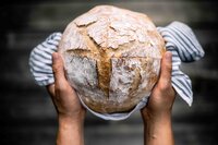 Warm image of hands gently holding sourdough loaf, symbolizing community support and charitable giving.