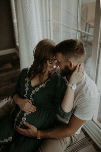 Couple cozies up on the floor in front of their big picture window, anxiously awaiting the arrival of their first babe.