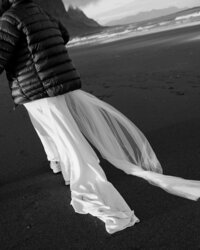 Black and white photograph of a bride in a flowing wedding dress walking along Stokksnes Beach, captured by a destination elopement photographer in Iceland.