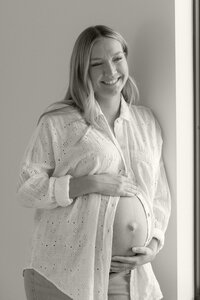 expecting mom smiling next to window at maternity photo session