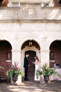 the bride and groom read their private vows to one another outside of their  wedding venue under a tall arch