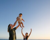 family of three tossing baby son in the air at waimanalo beach