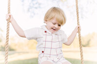 Young boy in a subtle plaid Christmas outfit swings from a rope swing during a family session.