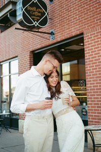 Candid photo of couple hugging and laughing holding coffee in downtown Loveland during their engagement session.