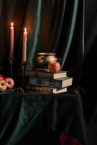 Stack of books next to apples and lit candlesticks with a green velvet backdrop.