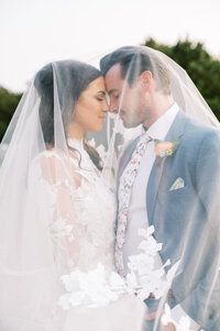 Bride and groom with heads touching romantically under the bride's veil