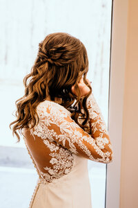 Bride facing away from the camera showcasing her hair while putting in her earrings before the ceremony