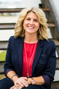 Blonde realtor smiles for headshots in red blouse and navy blazer outdoors on staircase