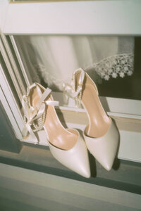 Bride's shoes sit on windowsill with curtain reflected in the window.