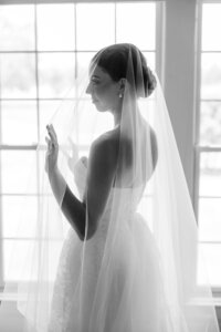 Bride in profile, standing by a window with veil.