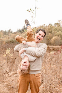 Dad holding son upside down both are laughing at the camera. Fall Family photo session Oregon.