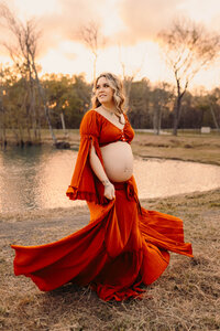 Maternity photography in Cleveland TX - expectant mother holding baby bump in rust orange gown outdoors