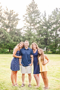 Family of four smiling at the camera while stand cuddling with each other at Wegerzyn Gardens in Dayton, Ohio.