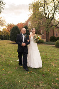 A bride is being lead down the isle by her father on her wedding day at the Manor House of Kings Charter.