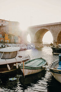 Golden sunlight spilling over a quiet European harbor, boats nestled against charming stone arches.