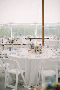 The interior of a tented wedding venue with white tables, white chairs, and floral arrangements 