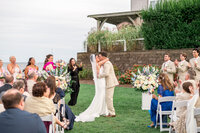 A bride and groom share their first kiss surrounded by colorful florals during an outdoor ceremony at Wychmere Beach Club in Cape Cod. A picture-perfect coastal wedding moment.