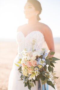 A bride taking a moment to showcase her floral bouquet as she stands in the middle of Eldorado Dry Lake Bed just outside of Las Vegas, Nevada.