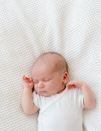 A newborn baby boy wearing white on a white blanket, taken by Amsterdam photographer, Sim Sawyers.