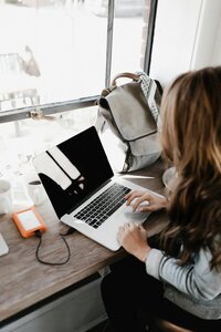 Woman sits at a bar in front of a window working on her computer. 