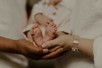 Deux paires de mains parentales tiennent délicatement les pieds d'un bébé lors d'une séance photo en Vendée.