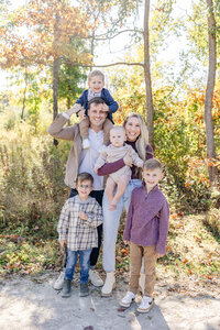 Mom holding baby and dad holding toddler on his shoulders, everyone smiling at the camera at a park in Centerville, Ohio.