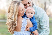 A mom and dad snuggling with their baby girl at Burke Lake Park at sunset.