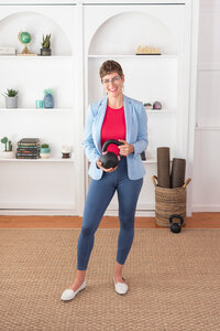 A woman in yoga attire holding a dumbbell and smiling.
