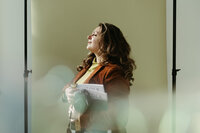 Sara Dobbins holds magazines while standing sideways and closing her eyes. A light flare appears in the foreground