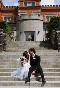 happy young couple kissing, sitting on stairs at destination wedding after ceremony