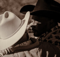 LGBTQ+ cowboys sit together in mismatched cowboy hats in a field during the sunset.