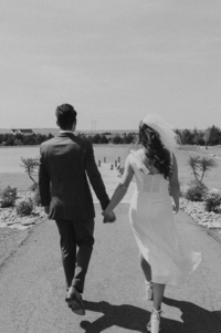 The groom and the bride are holding hands and walking on the pier,