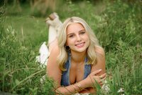 blonde charlotte senior lays in grass wearing a denim vest and skirt with boots during her senior portrait session