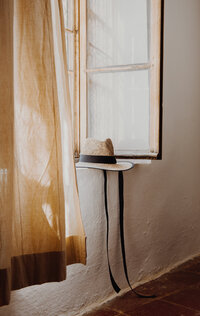Window with tan curtains and a hat on the ledge 