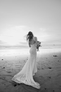 The back of a bride, showcasing the back of her dress while she stands holding her bouquet. 