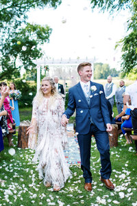 First time walking out as husband and wife at an outdoor wedding ceremony, with the crowd cheering and throwing petals. They radiate joy and celebration at The Cottage Farmhouse, captured by a Minnesota wedding photographer.