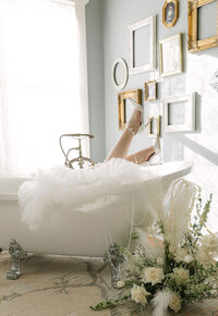 Bride laying in a clawfoot bathtub surrounded by white florals and wearing a dramatic tulle robe, photographed inside The Manor House for an editorial Colorado bridal portrait.