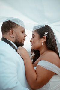 Bride and groom closing their eyes with bride's veil over them