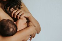 A woman holds her newborn baby while breastfeeding.