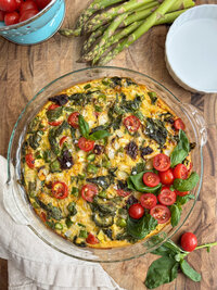 An asparagus frittata with cherry tomatoes and fresh basil in a glass dish.