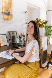 Creative Director Courtney Claire Beglin sitting at her desk in her studio smiling at the viewer
