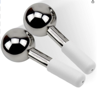 A pair of metallic silver facial ice globes with white handles, used for reducing puffiness and inflammation in the face. The globes are sleek, minimalist, and reflective.