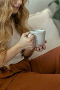 A woman named Anna Colwell, a therapist, sits on a couch, holding a coffee mug, exuding a calm and inviting presence.