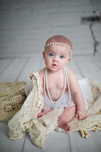 Adorable red-haired baby in studio session wearing string of pearls 