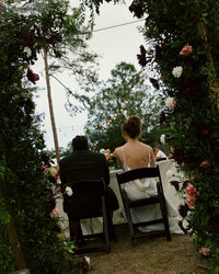 Ashley and Jordan sitting underneath a rose arch on their wedding day in North Port FL.