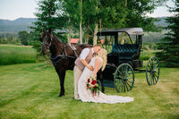 Jackson Hole wedding photographers capture Grand Teton wedding with couple kissing in front of horse drawn carriage